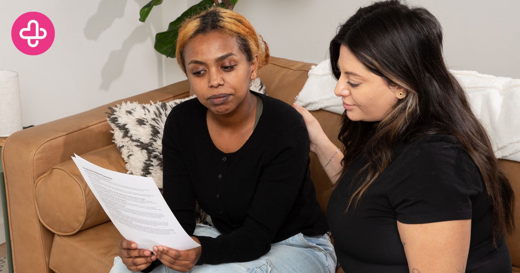 Two people sit on a couch; one reads a document while the other offers a supportive hand on their shoulder.